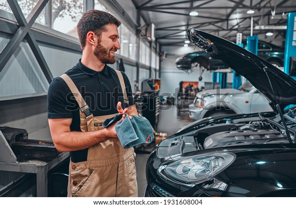 Mechanic wipes his hands after repairing the car.\
Side view.