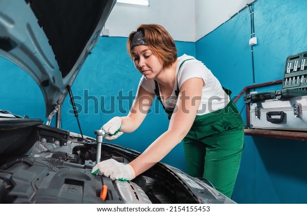 Mechanic woman in\
green coveralls repair a engine. The concept of woman\'s equality\
and works at auto repair\
shop.