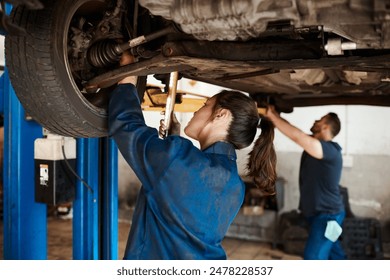 Mechanic, woman and man under car in workshop for auto repair, service and inspection for safety. Engineering, partnership and teamwork for vehicle maintenance with tools, parts or industry at garage - Powered by Shutterstock