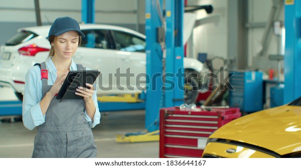 Mechanic woman with
tablet walking along car workshop. Car service, repair, maintenance
and people concept.
