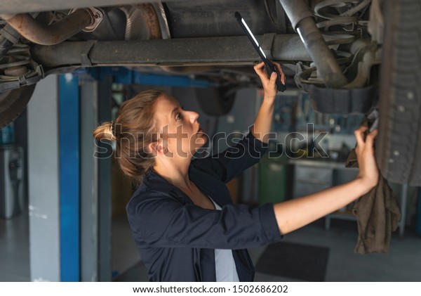A Mechanic woman\
working on car in her shop. Auto car repair service center.\
Portrait of smiling young female mechanic inspecting a CV joing on\
a car in auto repair shop
