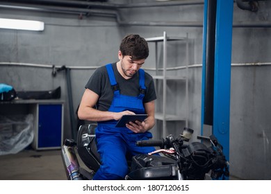 A mechanic in work clothes is sitting on a motorcycle. He uses a tablet - Powered by Shutterstock