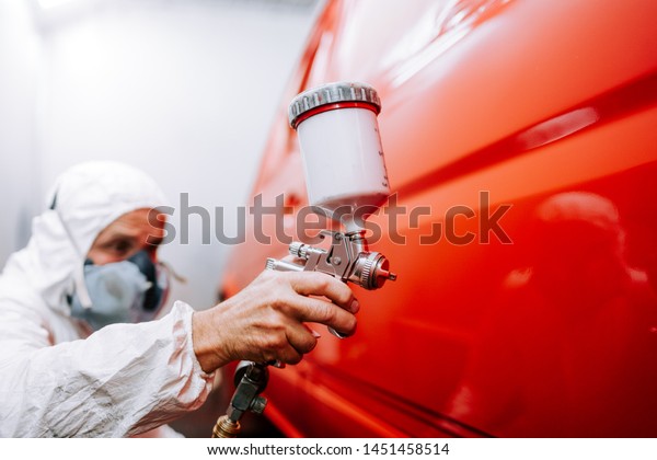 mechanic worker painting\
a car in a special painting box, wearing a full body costume and\
protection gear
