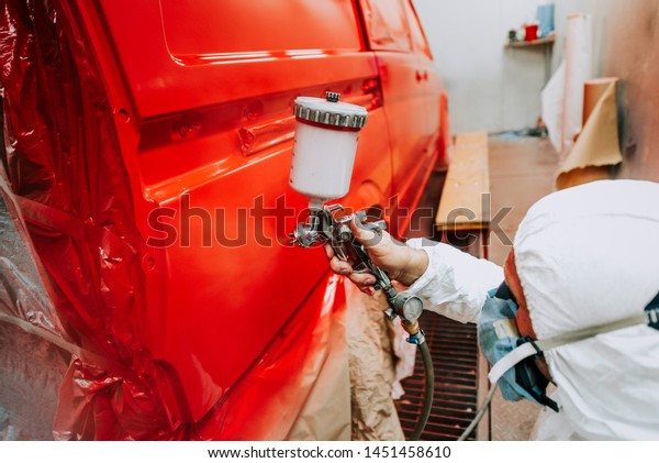 mechanic worker painting a\
car in a special painting box, wearing a white costume and\
protection gear