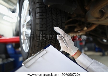 Mechanic worker point at tyre and write down in document notes
