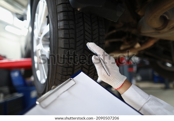 Mechanic worker point at tyre and write down in\
document notes