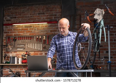 Mechanic working in a bicycle repair workshop consulting his laptop as he holds the loose wheel of the bike resting on a workbench - Powered by Shutterstock