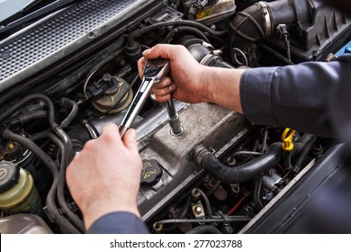 Mechanic working in a car under the hood, repairing an engine