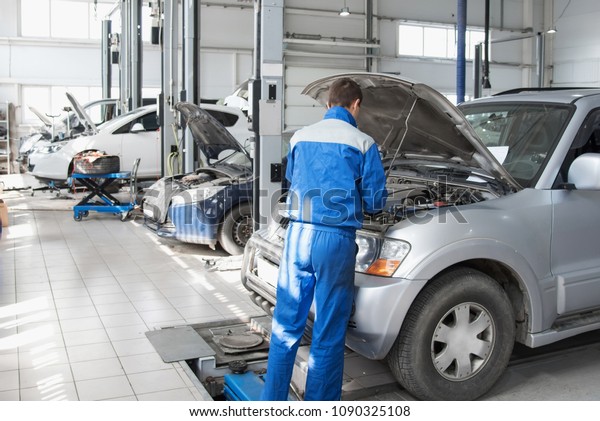 A mechanic working in\
a car workshop in a blue working form is repairing a gray car. Auto\
service.