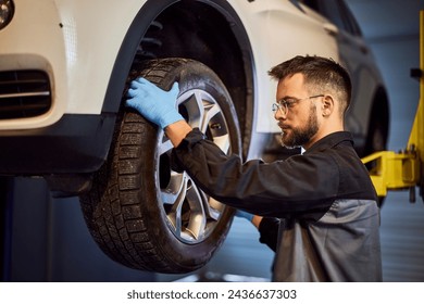 A mechanic working in his garage, checking a tire on a lifted car, wearing protective gloves. - Powered by Shutterstock