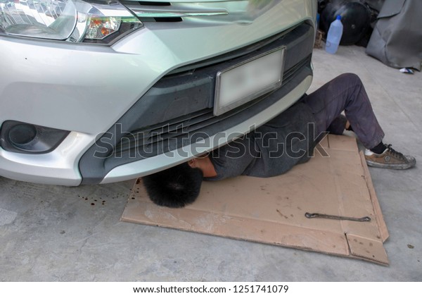 mechanic is working and lying under car to\
maintain car in garage