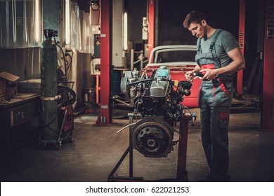 Mechanic Working On Classic Car Engine In Restoration Workshop