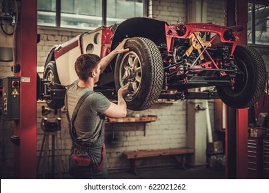 Mechanic Working On Classic Car Wheels And Suspension In Restoration Workshop