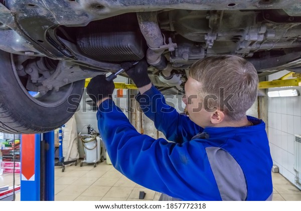 Mechanic\
working under a car at the garage. Technician wearing blue coverall\
and using a wrench. Car is on a hydraulic\
lift.