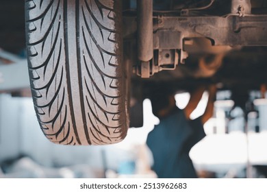 A mechanic working underneath a vehicle in a garage, focusing on a close-up view of a car tire in the foreground.
 - Powered by Shutterstock