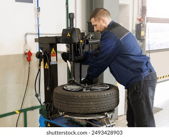 Mechanic works in tire repair shop. Car service mechanic puts wheel on car rim using special device. Replacing winter tires in workshop garage - Powered by Shutterstock