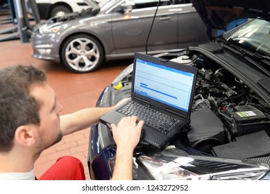 Mechanic In A Workshop Checks And Checks The Electronics Of The Car - Software Update With A Modern Computer 