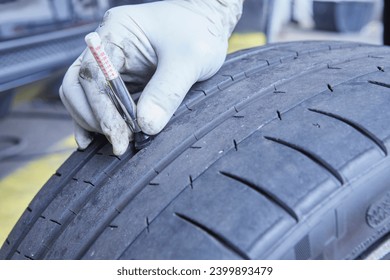 Mechanic in a workshop measuring the depth of a wheel tread. Inspection, review.