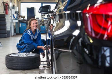Mechanic, A Young Woman Changing The Front Tire Of A Black Sedan Using A Torque Wrench In A Tire Service Center Garage