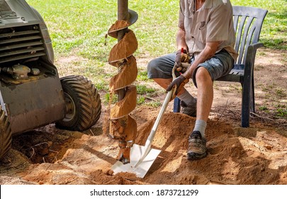 A Mechanical Auger Digging Holes In The Soil With The Aid Of A Senior Male With A Shovel