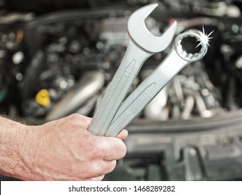 A Mechanical Of A Car Service Workshop Hold Some Tools In Front Of The Open Bonnet Of A Car And You See The Motor Engine In The Background