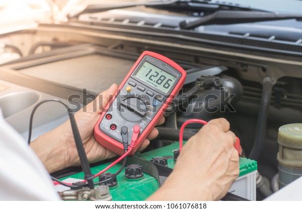 Mechanical car technician  hand\
checking voltage battery with multimeter in auto repair\
service.
