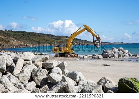 Mechanical diggers on a beach construction site repairing coastal defences and sea walls with rocks from a quarry after rising sea levels caused erosion and damage