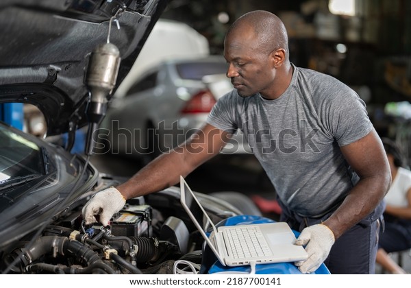 Mechanical
dirty face guy wearing half overall suit using USB Electonic
control unit ECU cable plug to engine perform programing and coding
tune up machine at garage car repair shop

