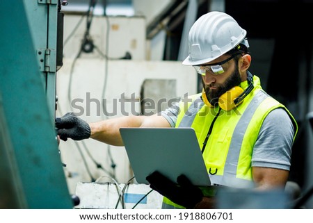 Mechanical engineer is setting up the control panel and looking the system in the laptop to check security in the control room at the factory.