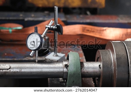 Mechanical engineer using dial indicator gauge to measure shaft runout and alignment on industrial machine in workshop.
