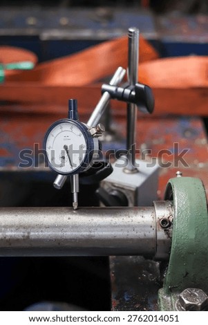Mechanical engineer using dial indicator gauge to measure shaft runout and alignment on industrial machine in workshop.