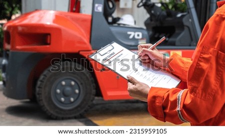 A mechanical engineer is using heavy equipment checklist form for inspecting the factory forklift vehicle (as blurred background). Industrial working with safety practice concept, selective focus. 