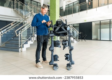 Mechanical exoskeleton computer engineer looking at the robot with a tablet. Physiotherapy in a modern hospital: Robotic skeleton. Physiotherapy Rehabilitation Scientists, Engineers and Physicians