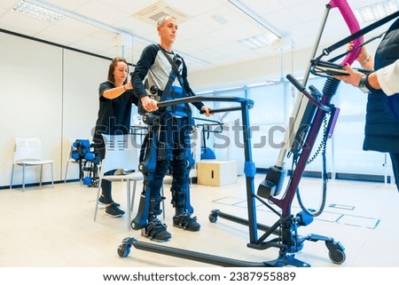 Mechanical exoskeleton. Female physiotherapy medical assistant lifting man with a disability with robotic skeleton. Futuristic rehabilitation, Physiotherapy in a modern hospital