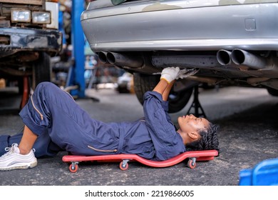 Mechanical girl dirty face wearing overall cover suit lay on garage creeper trolley tighten bolt under car at the car repair shop - Powered by Shutterstock