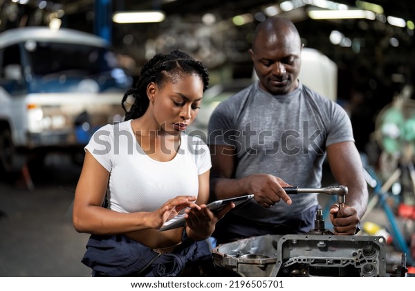 Mechanical girl wearing half overall cover suit\
hold wrench tighten and key information to tablet pc while talk\
with supervisor in training on vehicle inspection overhall engine\
transmission gear\
box\
