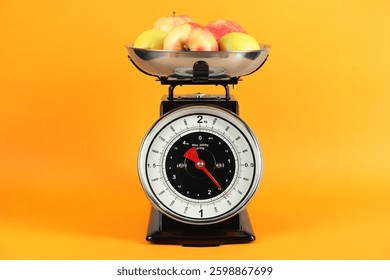 Mechanical kitchen scale with bowl of apples on yellow background