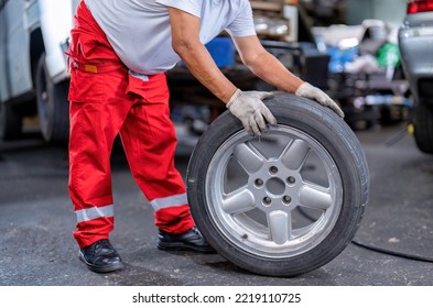 Mechanical Man Standing Roll Alloy Tire To Replace Flat Tire At The Car Repair Shop