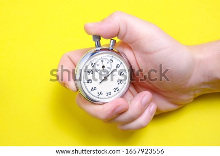 Mechanical stopwatch in a man's hand on a yellow background