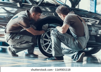 Mechanics Checking Wheel Bearings in Car Workshop. Two Professional Caucasian Adult Technician Master in Uniform in Front of Automobile in Garage. Repairing Car Service Concept