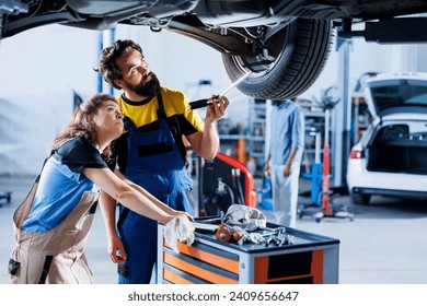 Mechanics collaborating on servicing broken vehicle, checking for faulty tires. Adept repairmen in auto repair shop working together on fixing car, discussing best options