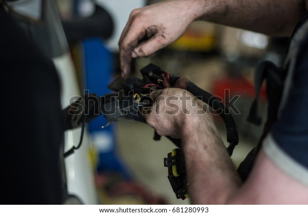 The\
mechanic\'s dirty hands hold wires and spare\
parts.