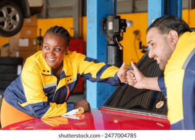 Mechanics giving thumbs up in auto repair shop. Male and female technicians in yellow and blue uniforms showing approval near red car. Positive teamwork in garage environment. - Powered by Shutterstock