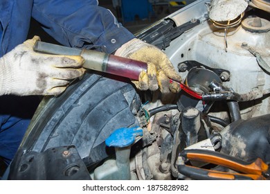 The Mechanic's Gloved Hands Hold A Syringe Of Red Oil. Replacing The Fluid In The Car's Power Steering System