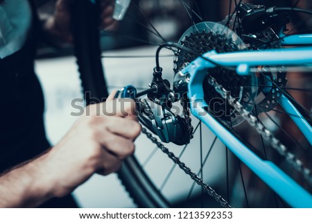 Mechanics Hand Repairing Bicycle in Bike Workshop. Closeup of Male Muscular Hand Examining and Fixing Modern Cycle Transmission System. Bike Maintenance and Sport Shop Concept