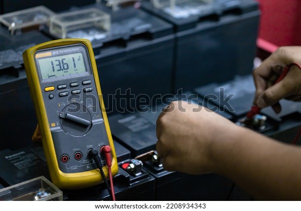 A mechanic\'s hand is using a multimeter to\
measure the voltage of the\
battery.