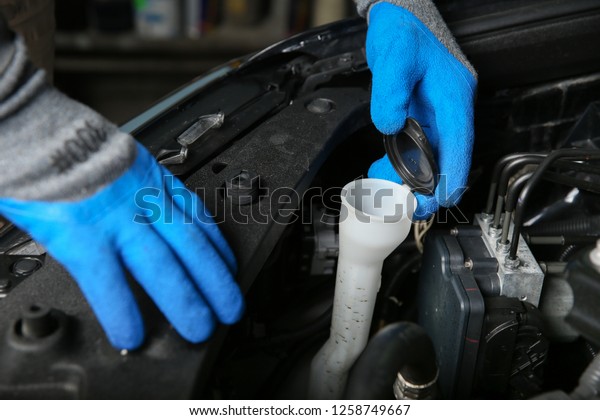 mechanic\'s hands in gloves are opening the\
windshield washer fluid reservoir in the\
car.