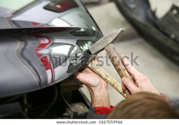 mechanic\'s hands straighten the car body.\
mechanic is aligning car body part by\
hammer