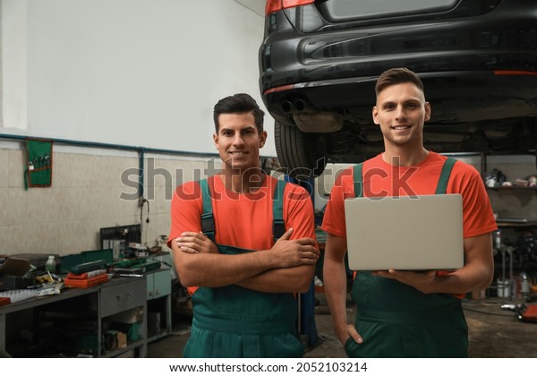 Mechanics with laptop near lifted car at automobile\
repair shop
