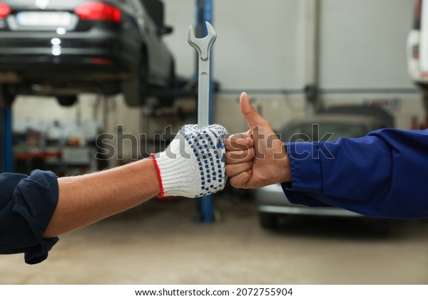 Mechanics making fist bump at automobile repair\
shop, closeup